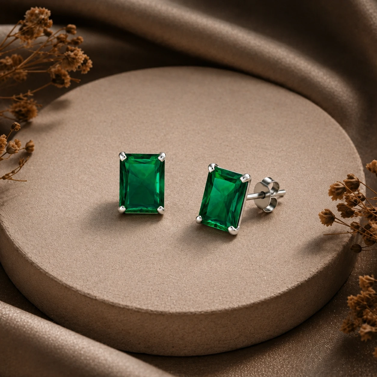 Emerald-cut green emerald solitaire studs securely claw-set in sterling silver.