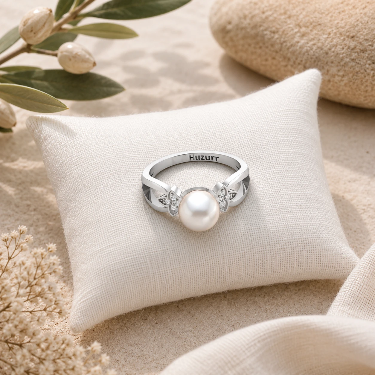 A silver ring featuring a round, white freshwater pearl, flanked by leaf designs studded with diamonds.