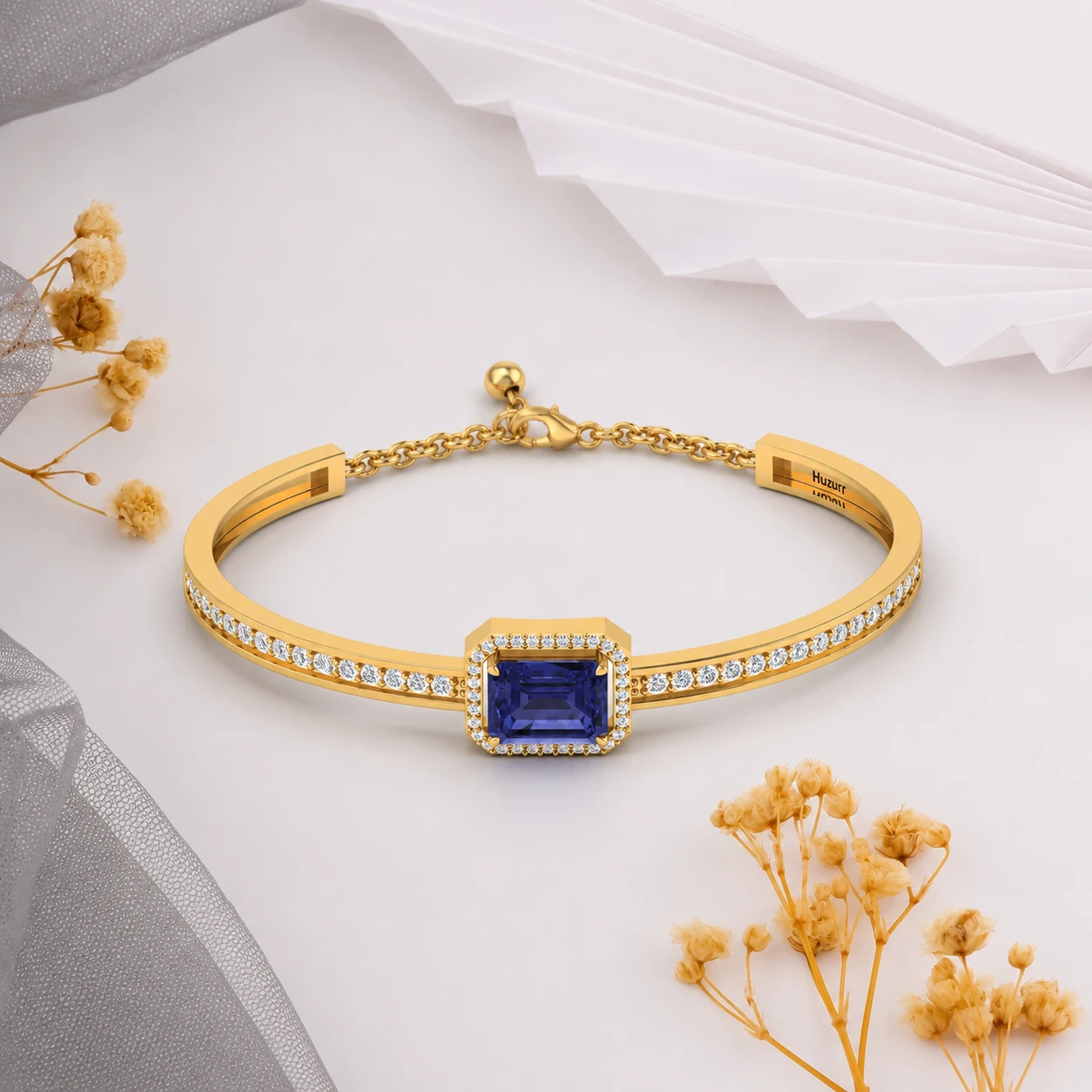 Three blue tanzanite gemstones surrounded by a diamond spiral on an open gold plated cuff