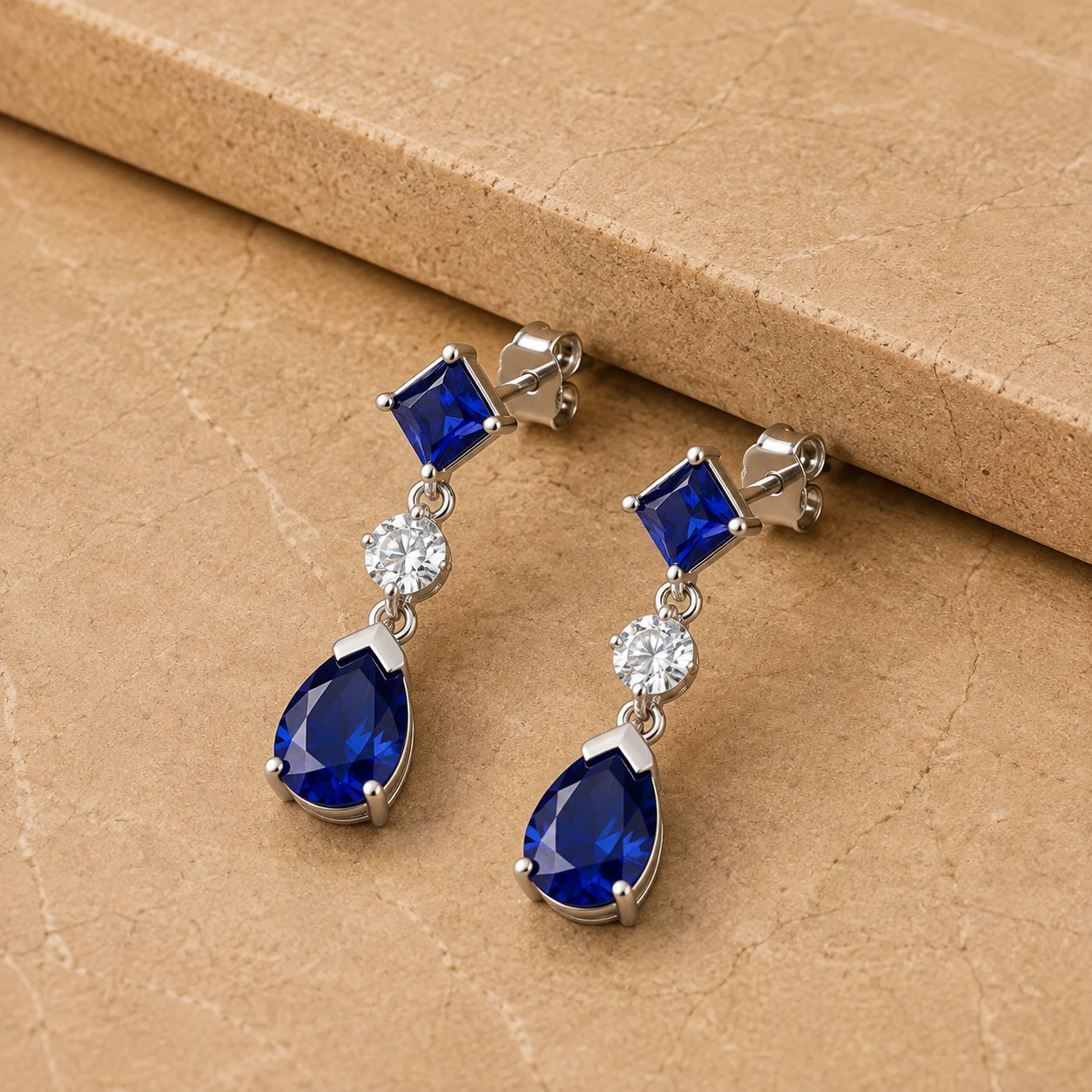 Linear silver earrings featuring princess and pear cut blue sapphires drop with diamond centers 