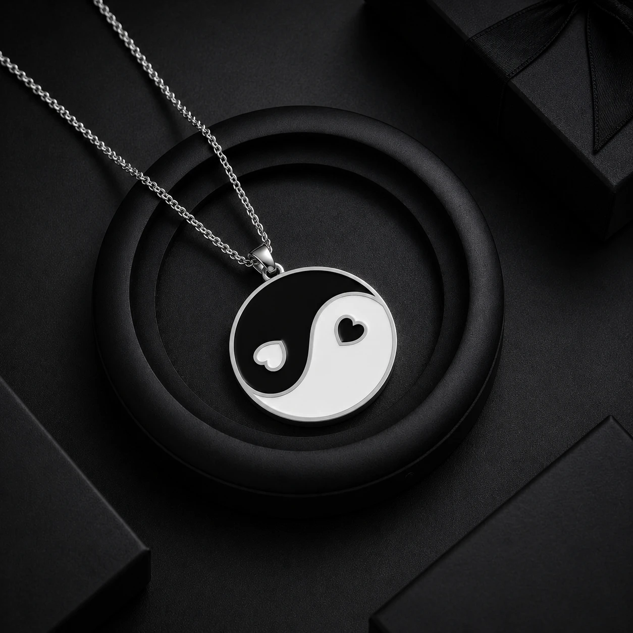 Circular silver pendant displaying a black and white enamel yin-yang symbol detailed with heart-shaped inner dots